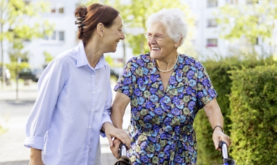 Eine jüngere Frau begleitet eine ältere Frau mit Rollator draussen beim Spazieren